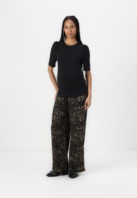 Crni uski top s kratkim napufanim rukavima, uparen s širokim hlačama od leopard printa u smeđoj i crnoj boji. Ravne crne cipele upotpunjuju outfita.