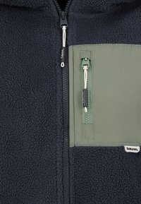 Fleecejack met een donkere marineblauwe kleur en een groene nylon zak, met ritsluiting en trekkoord. Textuurstof met gestikte details en branding.