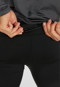 Zwarte sportleggings met een getailleerd ontwerp, voorzien van een discrete ritszak aan de achterkant en een gladde, stretchy stoftextuur.
