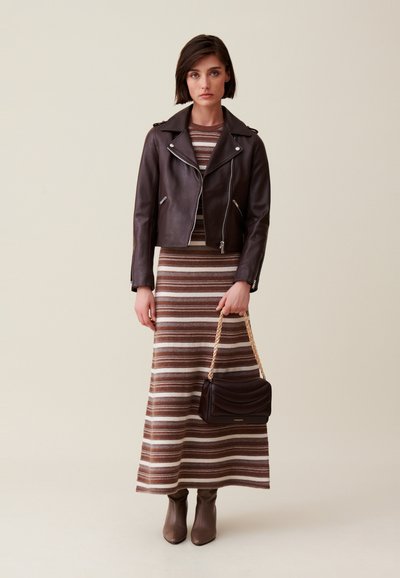 Veste en cuir marron de style biker, robe midi rayée marron et crème, bottes marron jusqu'au genou et un sac à main sombre avec une bandoulière en chaîne.