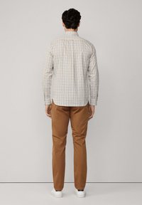 Camisa de cuadros de manga larga para hombre en blanco, azul y amarillo, con un diseño de cuello. Combinada con pantalones marrones y zapatos blancos.