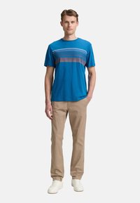 Blå kortærmet t-shirt med horisontalt stripemønster i grå og lilla, sat sammen med khaki-bukser og hvide sneakers. Glat stoftekstur.