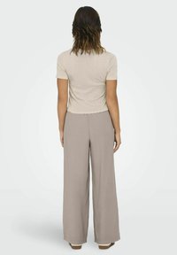 Beige cropped t-shirt parret med lysebrune vidde bukser, som viser en glat stofstruktur og en afslappet silhuet.