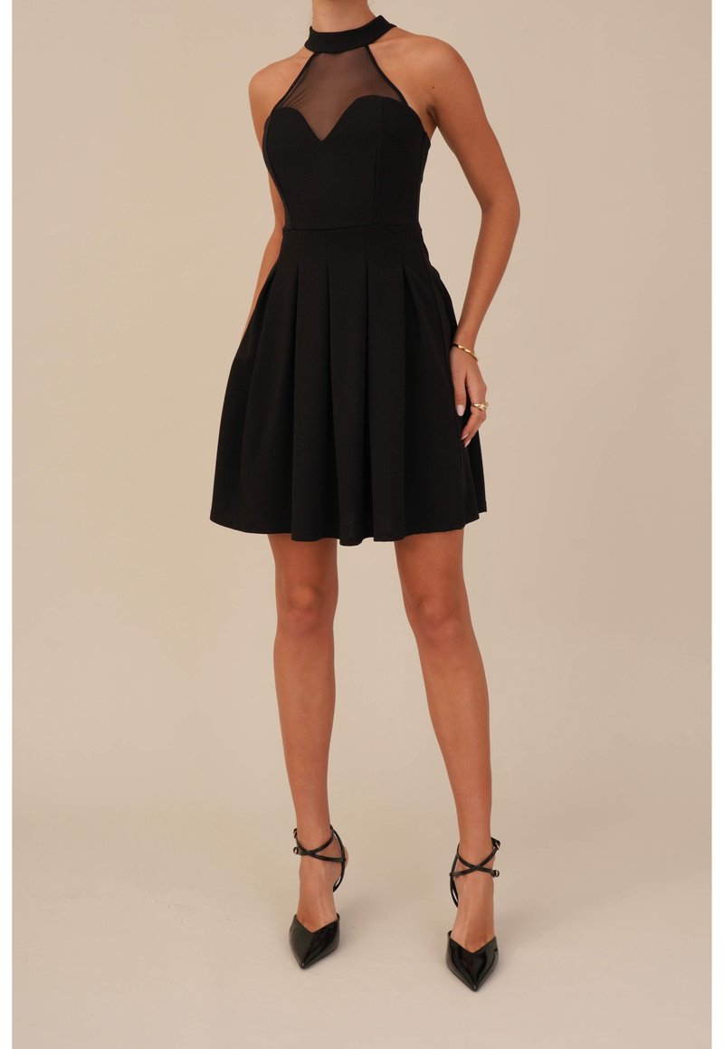 Robe noire avec un corsage ajusté, design à col halter et détails en filet transparent. Jupe évasée, longueur genoux, texture lisse, portée avec des talons noirs.