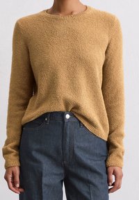 Mustard-colored knit sweater with a textured surface, round neckline, and long sleeves, paired with dark denim trousers.