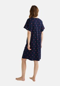 Robe de nuit marine avec une coupe ample, des manches courtes et un motif de petits cœurs rouges éparpillés partout. Tissu doux et léger.