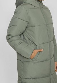 Abrigo largo acolchado verde con capucha, con costuras verticales, cremallera frontal, bolsillos laterales y puños elásticos para un ajuste ceñido.