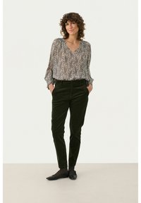 Bluse aus fließendem, transparentem Stoff mit einem schwarz-weißen Paisleymuster. Olivgrüne Cordhosen im Slim Fit mit Seitentaschen. Schwarze Ballerinas.
