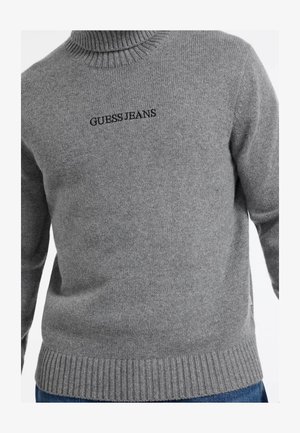 Gray knit sweater with a ribbed turtleneck and bottom hem. Features black embroidered "GUESS JEANS" logo on the chest. Smooth texture.