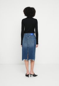 Farmer ceruzaszoknya rojtos szegéllyel, kék színben, középhosszú, hátul hasítékkal. Fekete magas sarkú papuccsal és fekete hosszú ujjú felsővel párosítva.