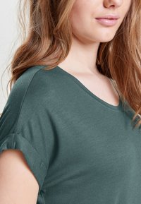 Dunkelgrünes T-Shirt mit kurzen Ärmeln, weichem Stoff und V-Ausschnitt, mit hochgekrempelten Ärmeln für einen lässigen Look.