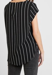 Blouse rayée noir et blanc à manches courtes, avec un col arrondi et un zip dans le dos ; tissu léger avec une coupe décontractée.