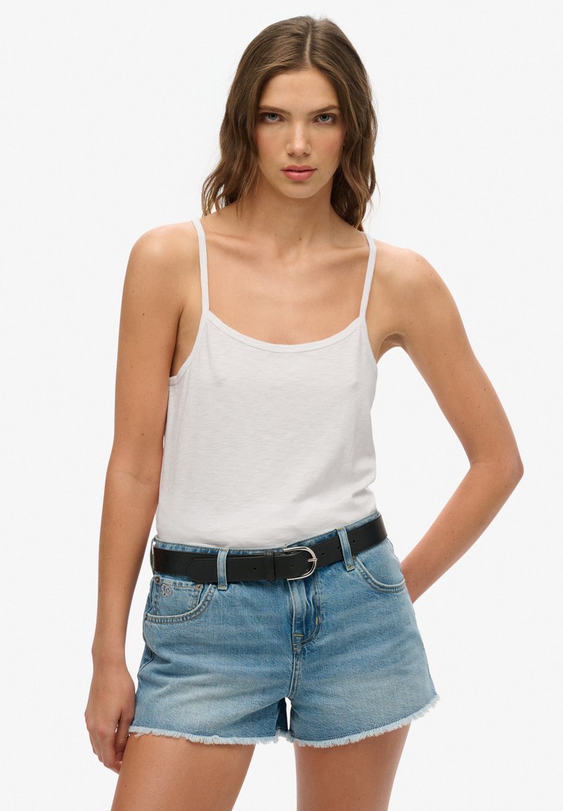 Witte katoenen tanktop met dunne bandjes, gecombineerd met lichtblauwe denimshorts met rafelige randen. Een zwarte leren riem accentueert de outfit.