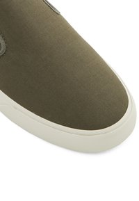 Olive-green canvas sneaker with a smooth texture, rounded toe, and white rubber sole. Features subtle stitching and a minimalist design.