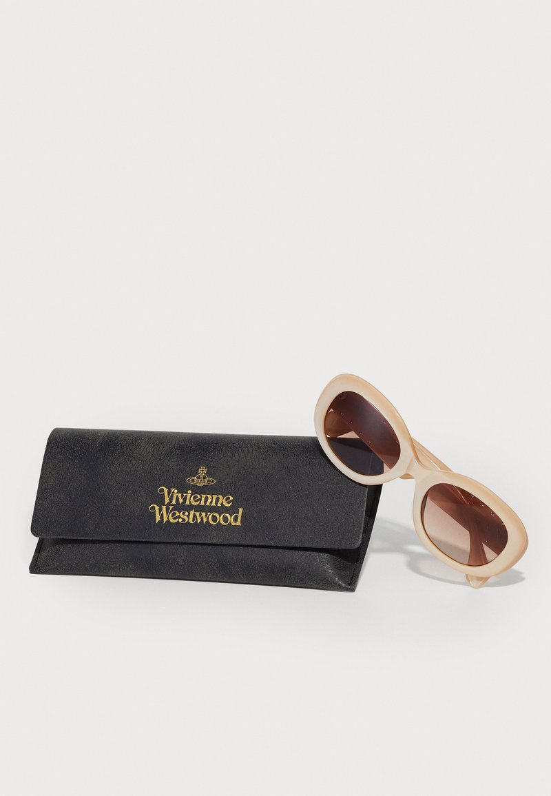 Vivienne Westwood solbriller i lys pink med brune linser, ved siden af et sort, struktureret etui med guld logo tryk.