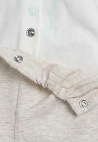 Tissu de couleur crème avec texture côtelée. Comprend des boutons-pression argentés et une ceinture élastique, mettant en valeur un matériau doux, respirant et un design pratique.