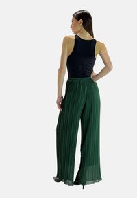 Groene geplooide wijde broek met een elastische tailleband, gecombineerd met een zwarte mouwloze top. Gladde stof met een vloeiende textuur en lange lengte.