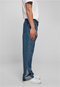 Lichtblauwe denim jeans met een rechte pasvorm, met een vervaagde textuur en kenmerkende zijsplitten aan de zoom. Draagt met witte sneakers.