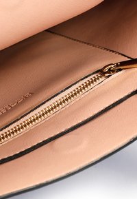 Hellrosa Lederinnentasche mit goldenen Reißverschluss und schwarzem Rand, zeigt Gewebestruktur und Nähdetails.