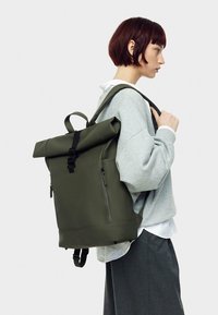 Roll-top backpack in olive green, made of water-resistant material, with adjustable straps, zippered pocket, and textured finish.