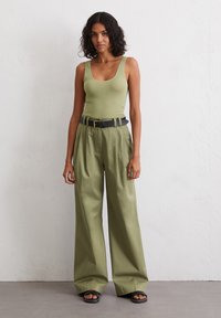 Olive green fitted tank top with a scoop neckline, paired with loose, high-waisted olive trousers and a black belt. Black slide sandals.