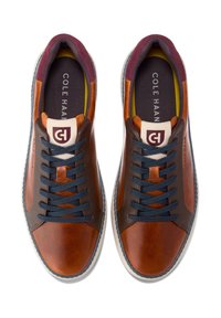 Hnědé kožené tenisky s tmavě hnědými akcenty, námořnickými šněrovadly, bílou podrážkou a polstrovaným burgundským límcem. Logo na jazyku a stélce.