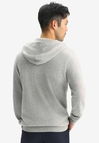 Grå hoodie med dragsko, mjuk textur och ribbad manschett och nederkant, sedd bakifrån. Avslappnad design med en lös passform.