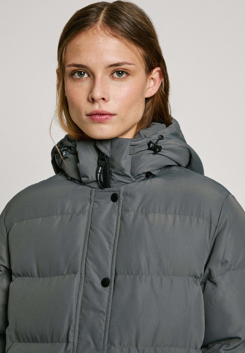 Giacca puffer grigia con chiusura a zip e bottoni automatici, dotata di cappuccio regolabile, texture trapuntata e finitura liscia e lucida.