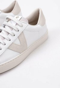 Baskets blanches en cuir avec des accents en suede beige, lacets plats et une semelle texturée. Design minimaliste avec une finition lisse.