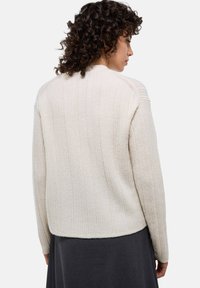 Pull en tissu côtelé de couleur crème avec un col rond et des épaules abaissées, présentant un motif texturé et une taille courte.