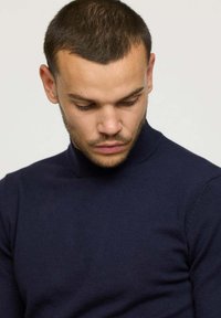 Pull à col roulé côtelé bleu marine, fabriqué à partir d'un matériau tricoté doux et texturé, présentant un design ajusté et un col haut.