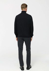 Fekete kötött garbó pulóver hosszú ujjakkal, szürke nadrággal és fekete cipővel párosítva, hátulról fényképezve, hangsúlyozva a textúráját és a szabását.