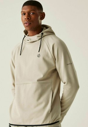 Man wearing beige hoodie with black drawstrings and DARE 2B logo on chest and sleeve, standing against light background.