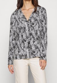 Langærmet skjorte med knapper i sort og hvidt prikkemønster, med V-udskæring og blødt stof, fremhævet med en afslappet pasform.