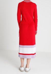 Roter gestrickter Pullover mit weißem gestreiftem Kragen, kombiniert mit einem ribbelten rot-weiß gestreiften Rock. Das Model trägt weiße Sneakers.