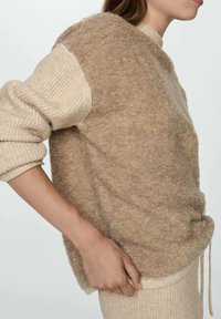 Langarmpullover aus weichem beigen Strick mit strukturiertem Körper, gerippten Ärmeln und einem leicht oversized Schnitt. Mit Kordelzug am Saum.