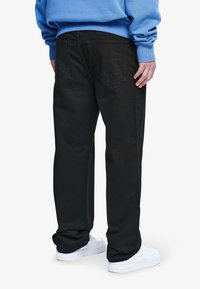 Pantalones de denim negro con un corte relajado, que cuentan con dos bolsillos traseros y una pierna ligeramente ajustada, combinados con zapatillas blancas y una sudadera azul.