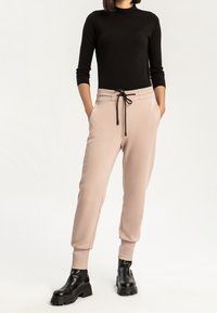 Ljusrosa joggers med elastisk midja, dragsko och sidofickor, kombinerat med en figurnära svart långärmad topp och svarta ankelboots.