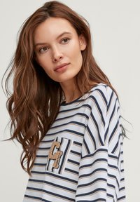 Camicia a maniche lunghe a righe con righe blu navy e beige, taschino con un'applicazione testurizzata a forma di "C" e una vestibilità rilassata. Tessuto di cotone.