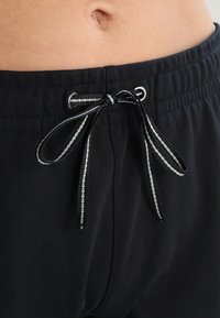 I pantaloni in cotone neri presentano una vita elasticizzata con un cordoncino in bianco e nero, evidenziando un design semplice e funzionale.