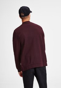 Burgundy sweatshirt made from soft fabric, featuring a round neckline and relaxed fit. Back view shows a plain design without embellishments.