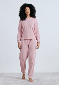 Σετ ανοιχτό ροζ ρούχα για χαλάρωση με μακρυμάνικη μπλούζα με κουμπιά στον λαιμό και παντελόνι με ελαστικές μανσέτες, φτιαγμένο από απαλό ύφασμα.