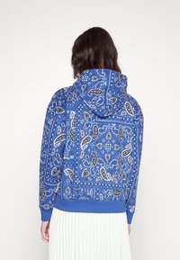 Felpa blu con un motivo paisley in bianco e nero, dotata di tasca a marsupio e polsini a coste al fondo e alle maniche.