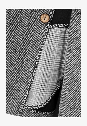 Grijze stof met een houndstooth-patroon en een houten knoop, voorzien van een zak met zwarte randen en een witte geruite voering.