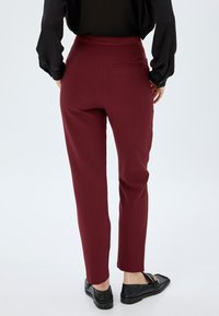 Bordeaux-kleurige op maat gemaakte broek met een gladde textuur, slim fit en achterzakdetails, gecombineerd met zwarte gestructureerde loafers.