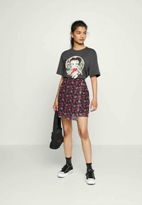 T-shirt gráfica preta com um personagem de desenho animado, combinada com uma saia transparente com estampado floral em tons de rosa e preto. Ténis pretos completam o visual.