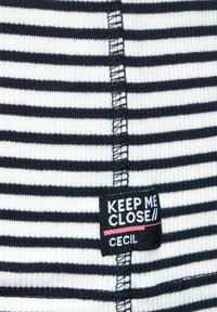 Proužkovaný top v námořnické modré a bílé barvě s žebrovanou texturou a středním švem. Obsahuje štítek s nápisem "KEEP ME CLOSE" a značkou "Cecil".
