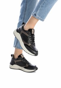 Zapatillas negras y grises con un upper de cuero texturizado, cuello acolchado y una entresuela blanca en contraste, mostradas en un pie con jeans azules.