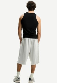 Zwarte mouwloze tanktop, losse witte shorts met zijzakken, gedragen met grijze sneakers en witte crew-sokken. Krullend haar zichtbaar van achteren.
