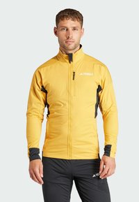 Yellow lightweight jacket with black accents, stand-up collar, zippered chest pocket, and fitted design suitable for outdoor activities.